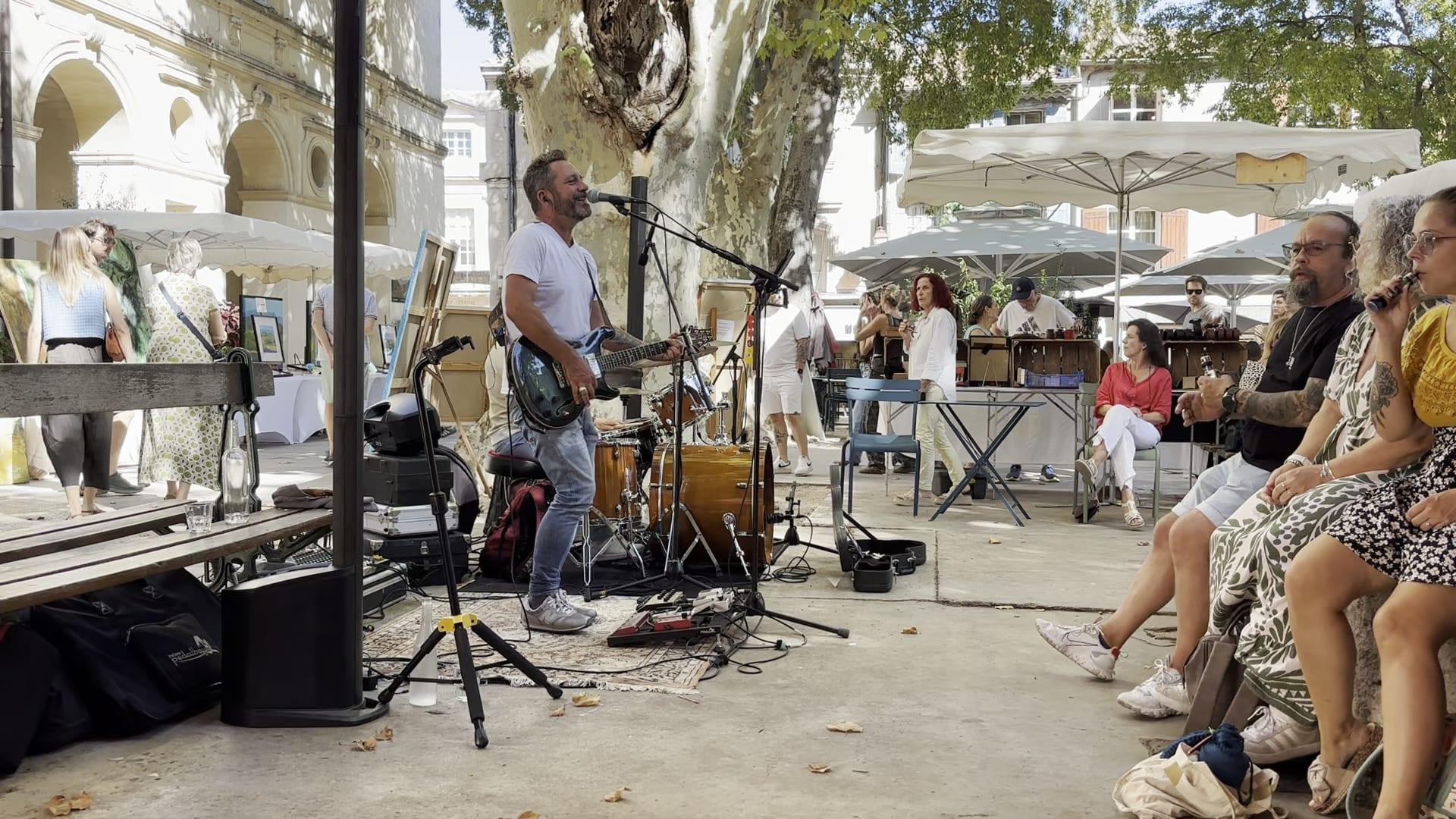 A musician singing and playing guitar beside café seating in Saint-Rémy-de-Provence.
